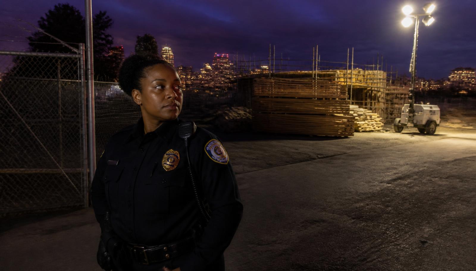 Summit Force officer holding a construction site gate at night with the Sacramento skyline behind
